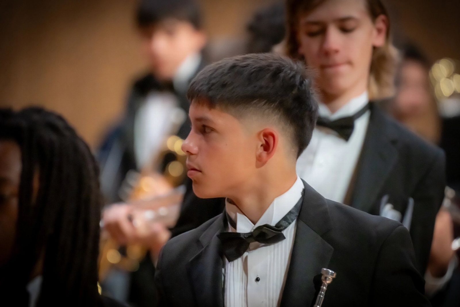 A young man in a tuxedo at a formal event, with guests behind him.