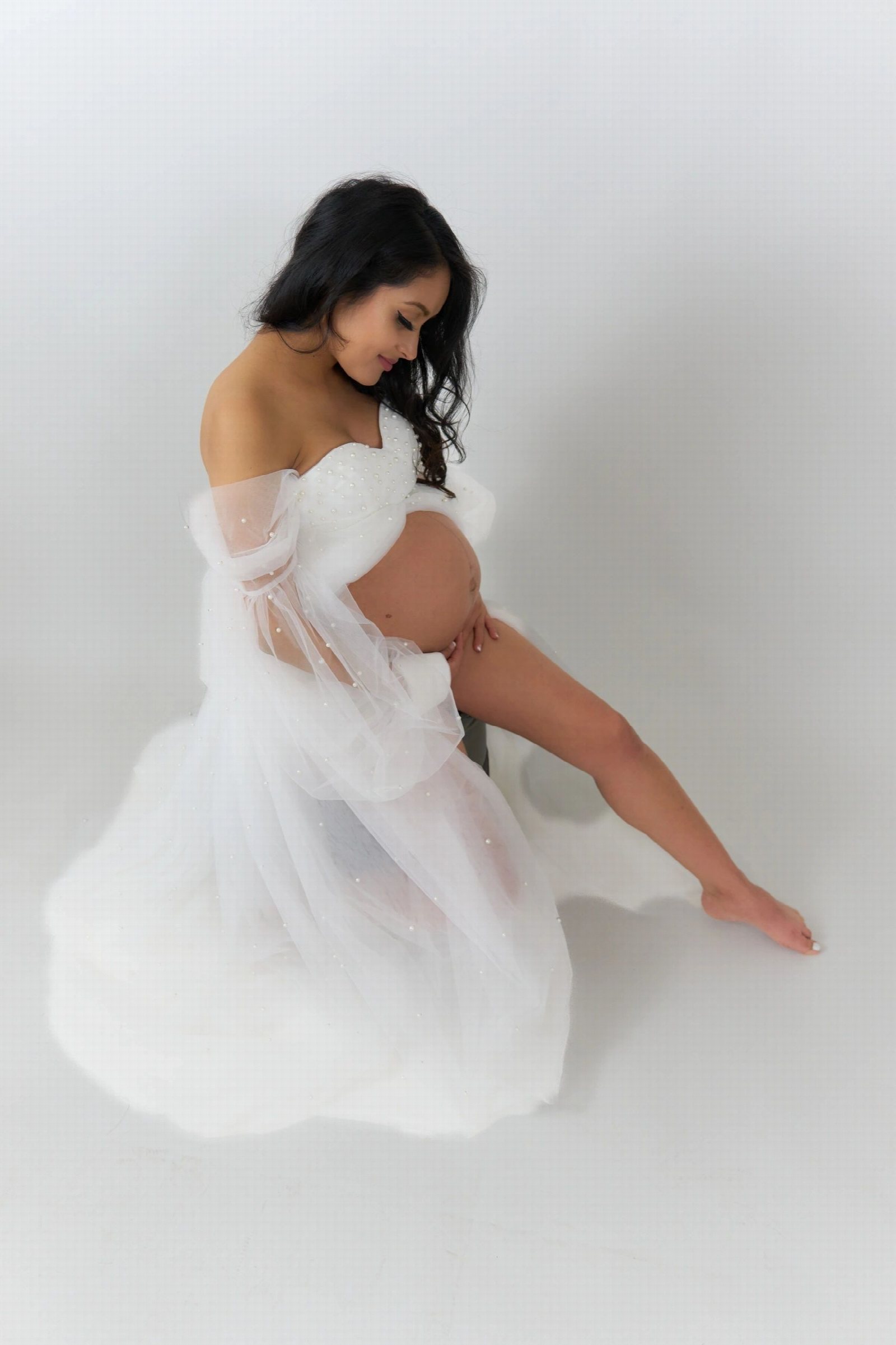 Studio maternity portrait of a woman in a flowing white gown.