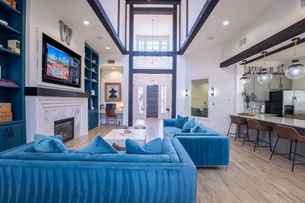 Open-plan living room with blue velvet sofas, exposed beams and a bar counter.